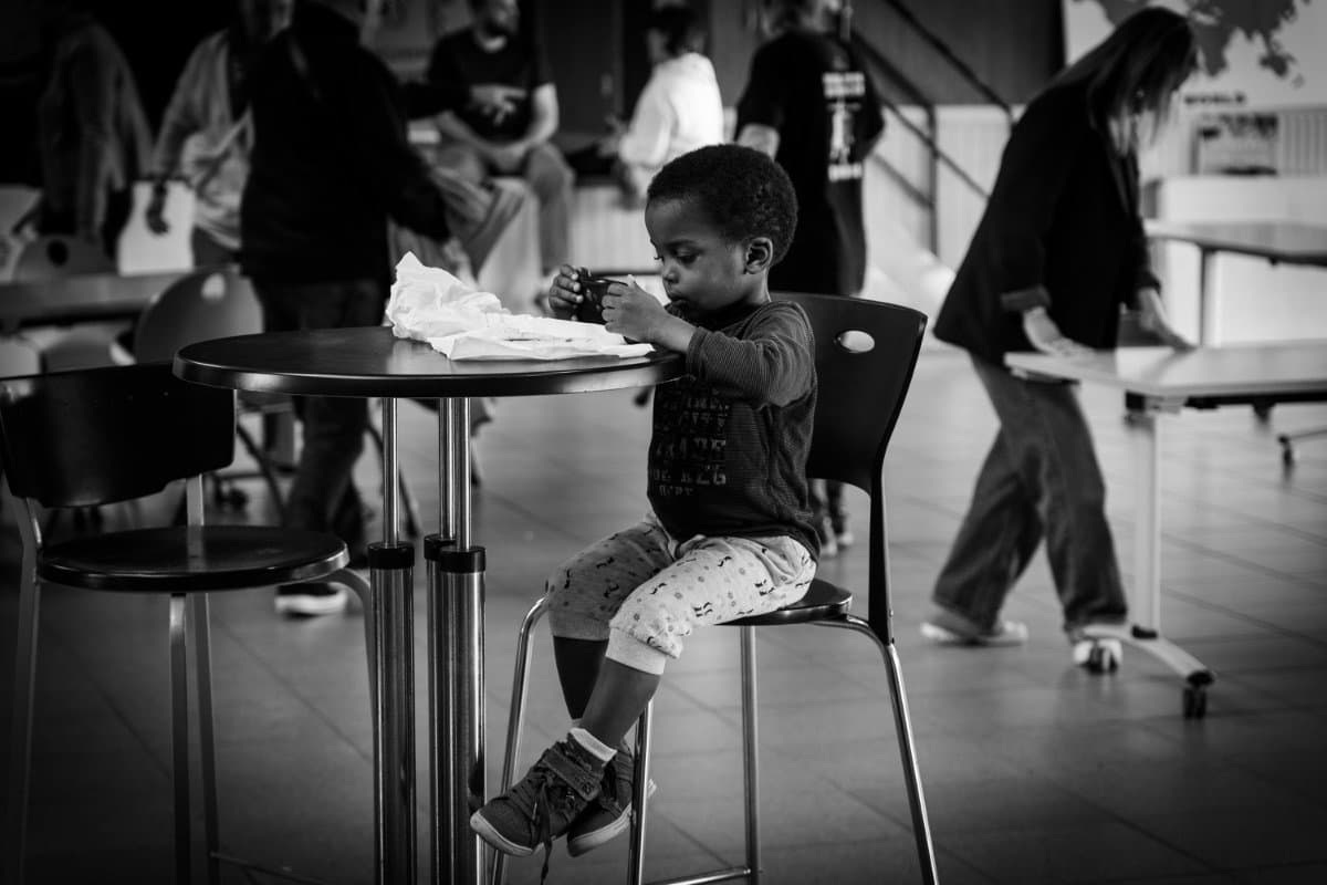 enfant assis à une table ronde dans un espace public intérieur en noir et blanc
